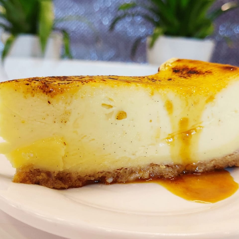 Slice of creamy caramel-topped cheesecake on a white plate, with caramel sauce drizzled over the crust and plate.